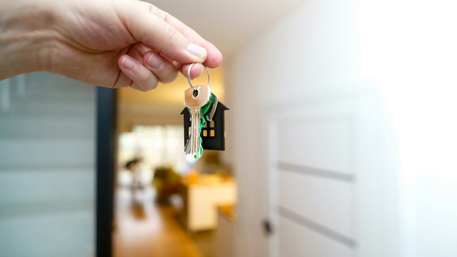 A hand holding house keys in front of an apartment entrance door