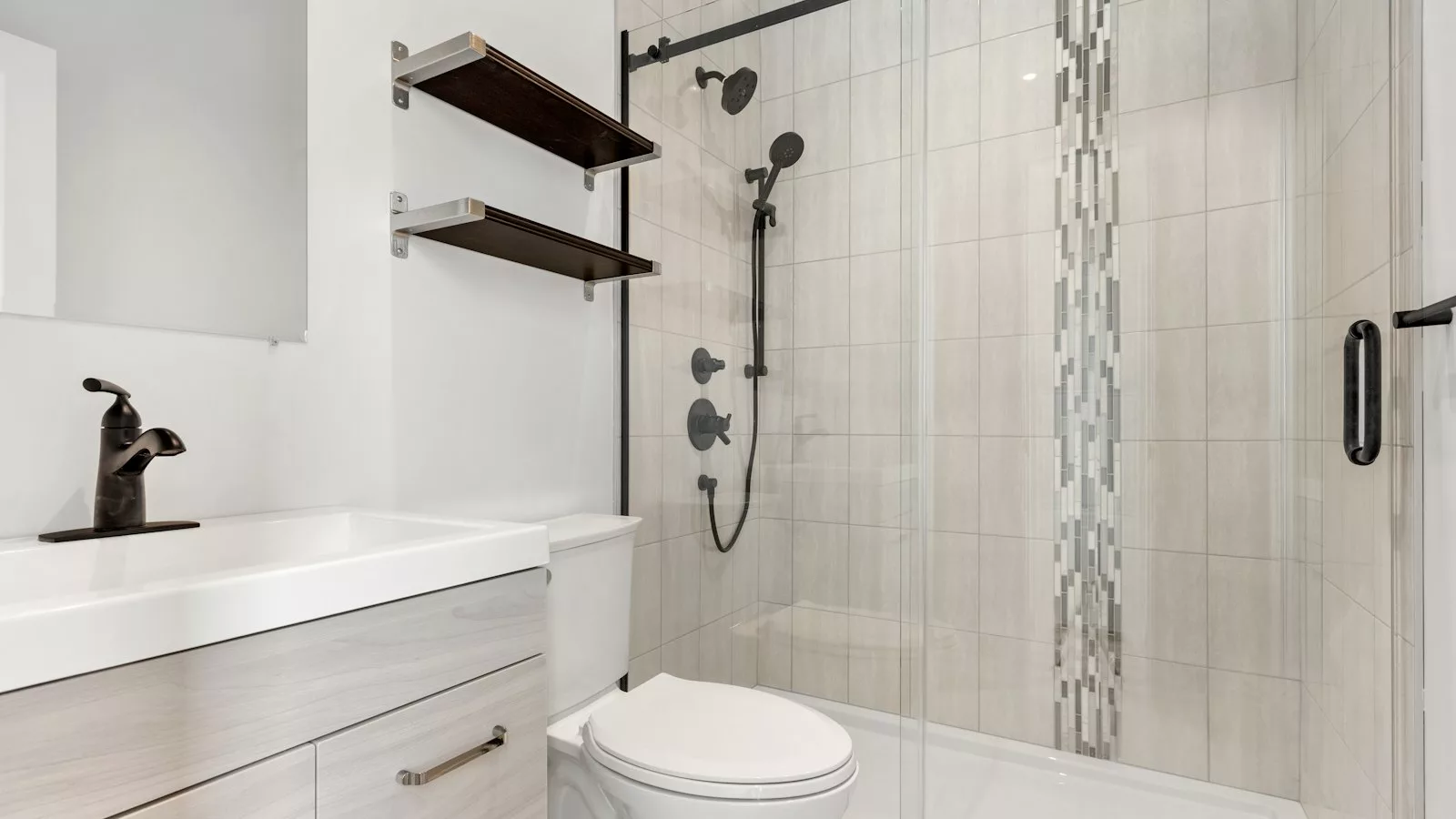 Small remodeled bathroom with a tiled walk-in shower behind a sliding glass door, a vanity and a toilet