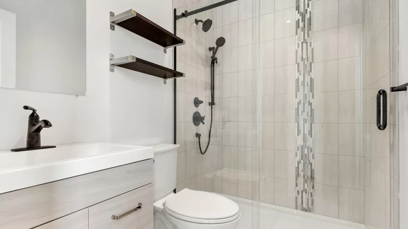 Small remodeled bathroom with a tiled walk-in shower behind a sliding glass door, a vanity and a toilet