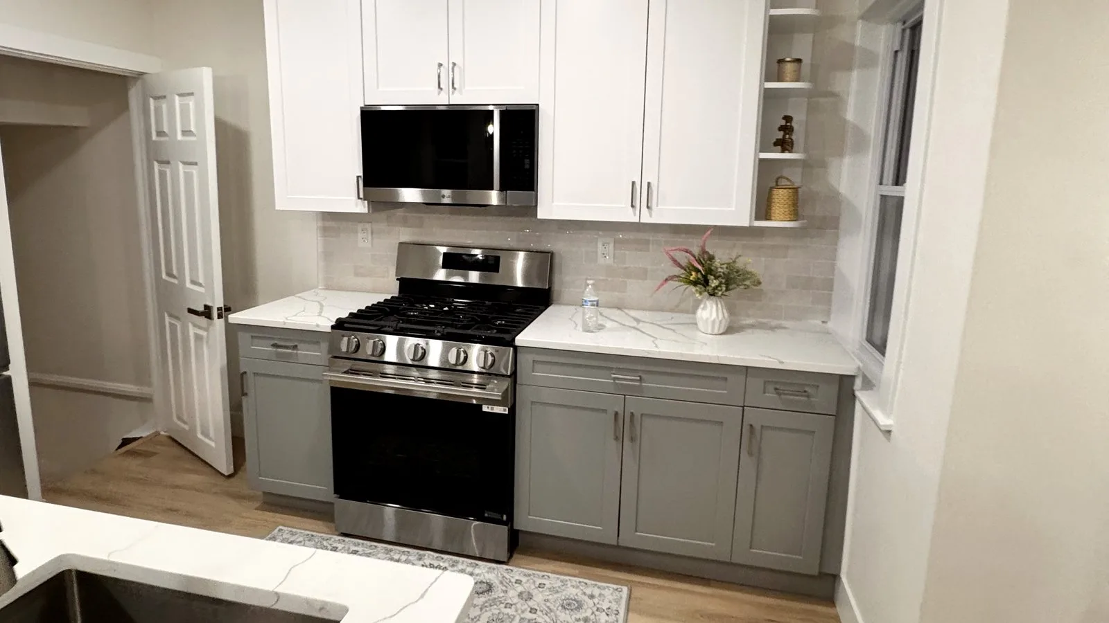 Remodeled rowhome kitchen with white upper and gray lower shaker cabinets, quartz counters and a stainless gas range