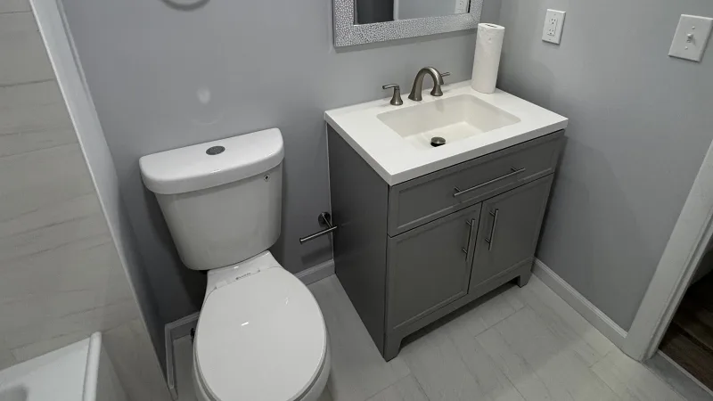 Remodeled bathroom with a gray shaker vanity, white top, brushed nickel faucet and light gray tile floor in Philadelphia
