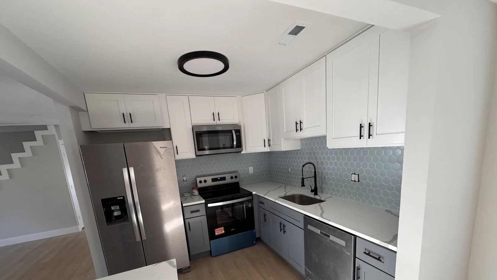 Two-tone kitchen with white upper and gray lower shaker cabinets, a blue hexagon tile backsplash and stainless appliances