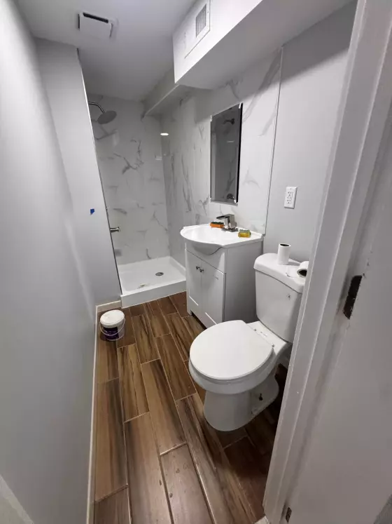 Bathroom with a marble-look tiled shower, white vanity and wood-look tile floor