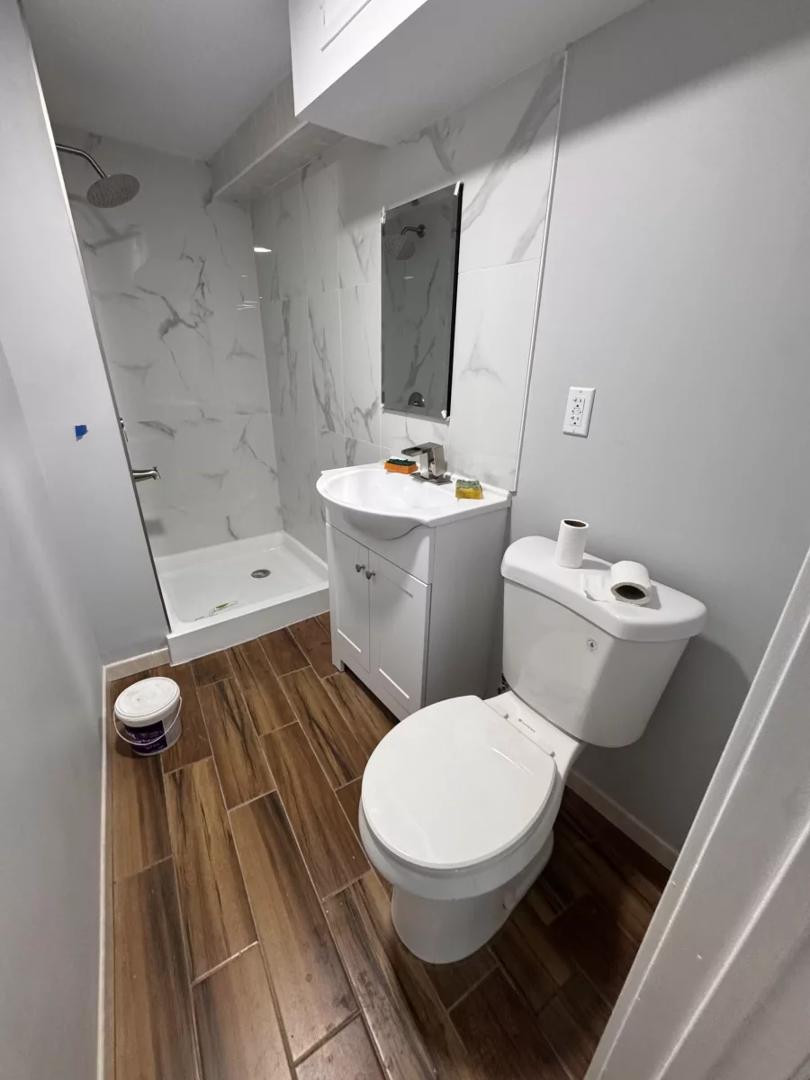 Shower with marble-look porcelain tile next to a white vanity and toilet