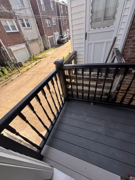 Rear deck with gray composite boards and black railings behind a Philadelphia rowhome