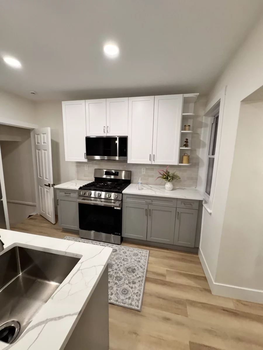 Kitchen with white upper cabinets, gray lower cabinets, quartz counters and a stainless gas range