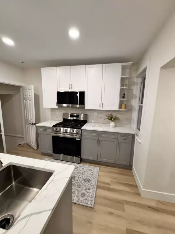 Kitchen with white upper cabinets, gray lower cabinets, quartz counters and a stainless gas range
