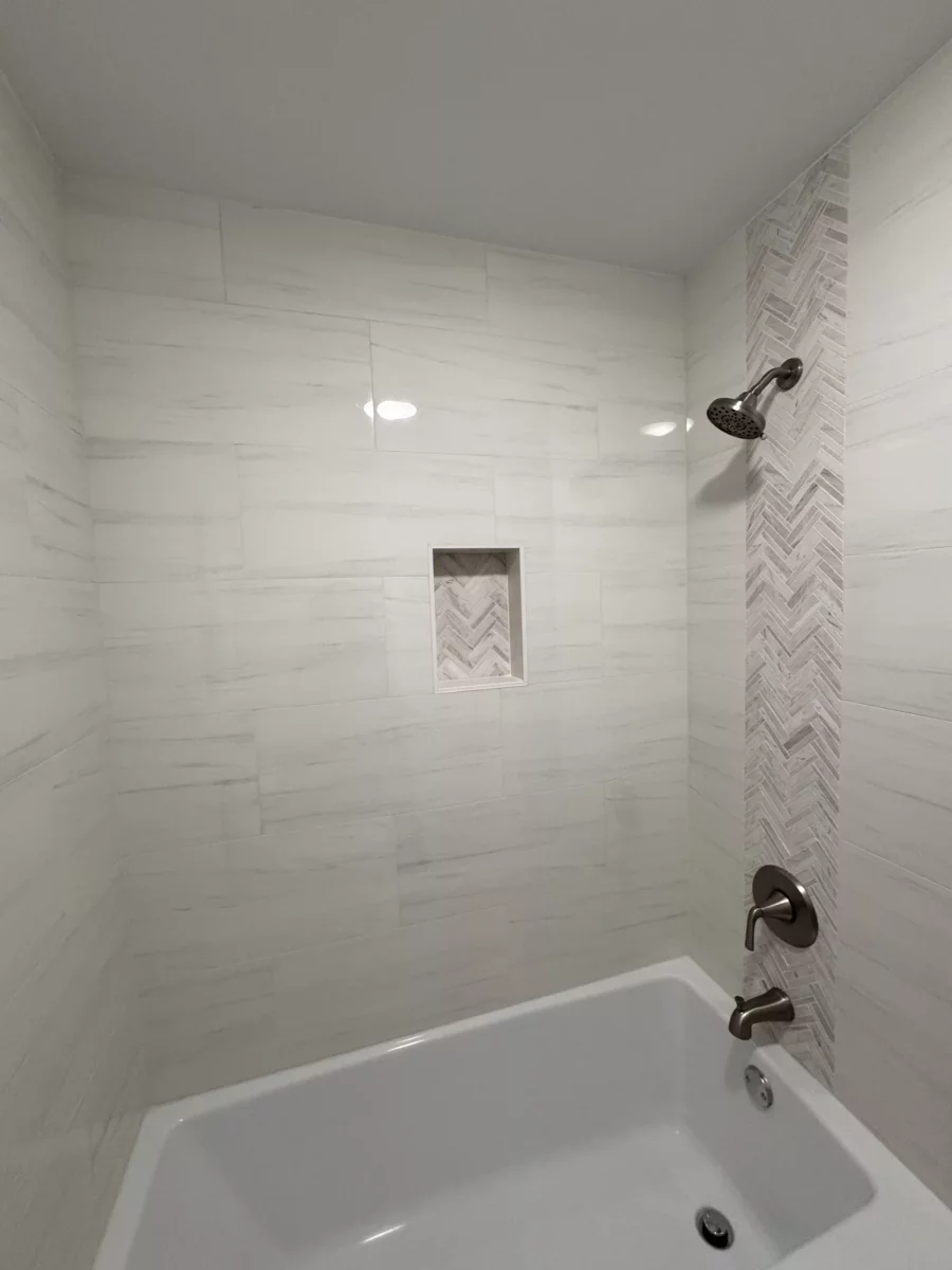 Tub and shower surround in white porcelain tile with a herringbone accent strip and niche