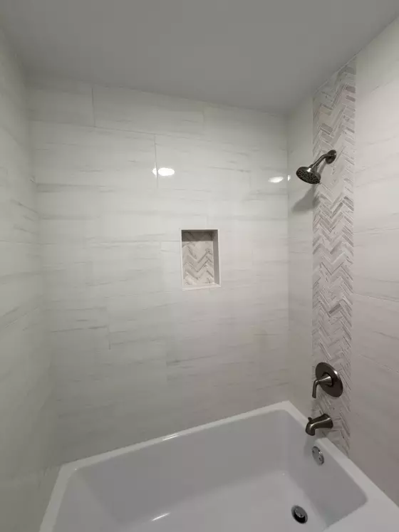 Tub and shower surround in white porcelain tile with a herringbone accent strip and niche