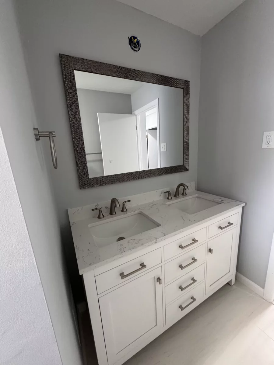White double vanity with marble top, brushed-nickel faucets and a framed mirror