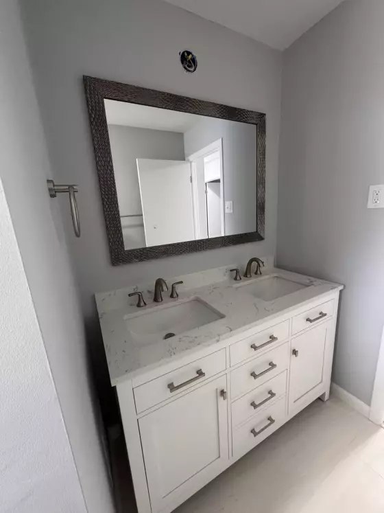White double vanity with marble top, brushed-nickel faucets and a framed mirror