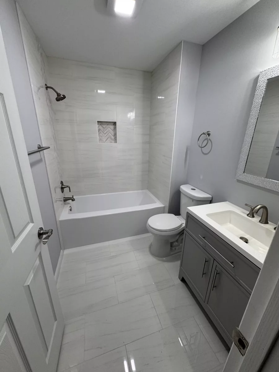 Bathroom with a gray vanity, white porcelain tub surround with herringbone niche and light gray tile floor