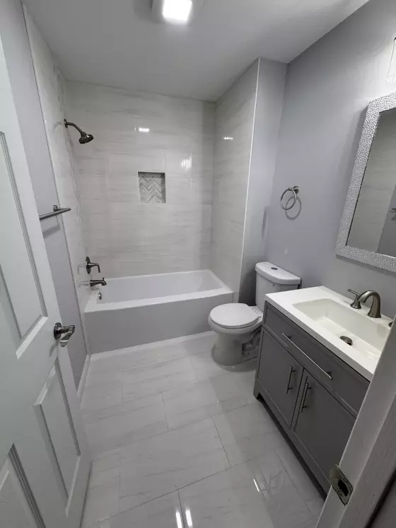Bathroom with a gray vanity, white porcelain tub surround with herringbone niche and light gray tile floor