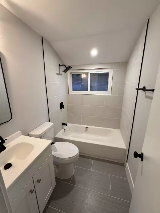 Bathroom with matte black fixtures, a white vanity, tub with tile surround and gray plank tile floor