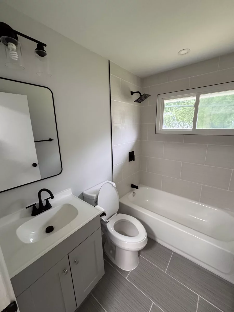 Bathroom with a black light fixture, white vanity, toilet and tiled tub surround