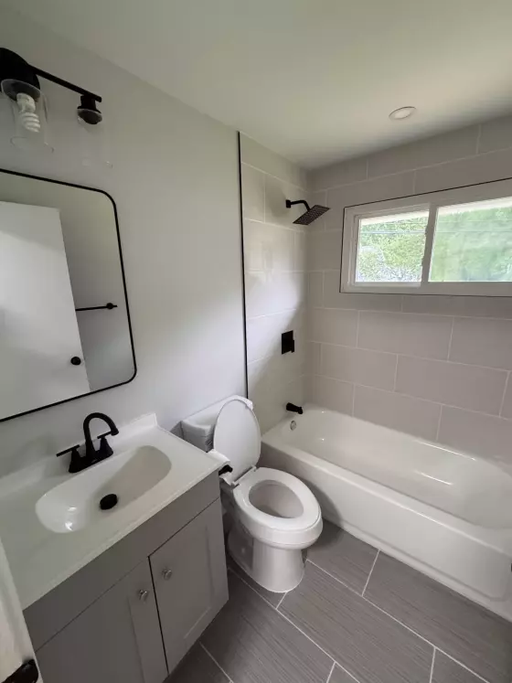 Bathroom with a black light fixture, white vanity, toilet and tiled tub surround