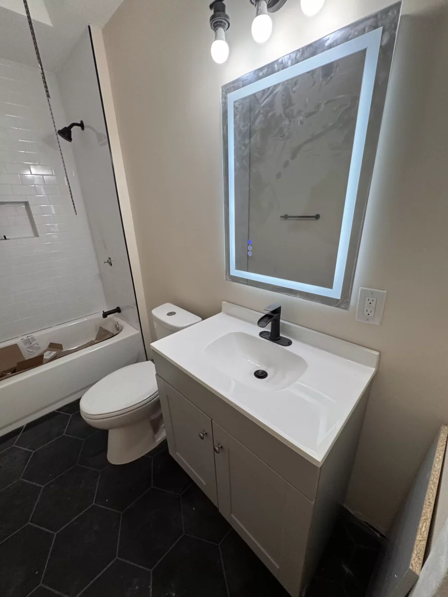 Bathroom with black hexagon floor tile, white vanity, lighted LED mirror and white subway tile tub surround