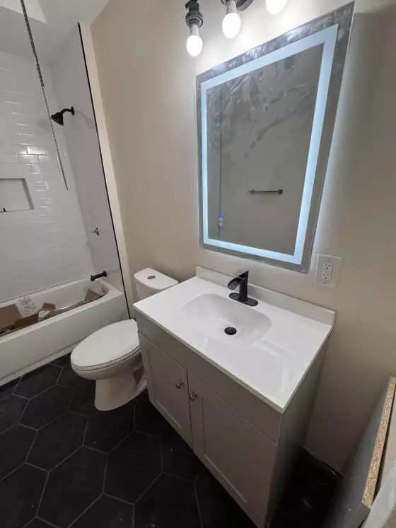 Bathroom with black hexagon floor tile, white vanity, lighted LED mirror and white subway tile tub surround