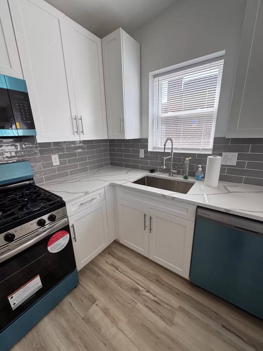 White shaker cabinets with an undermount stainless sink under a window and gray subway tile backsplash