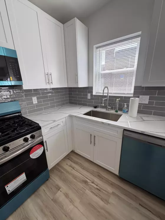 White shaker cabinets with an undermount stainless sink under a window and gray subway tile backsplash