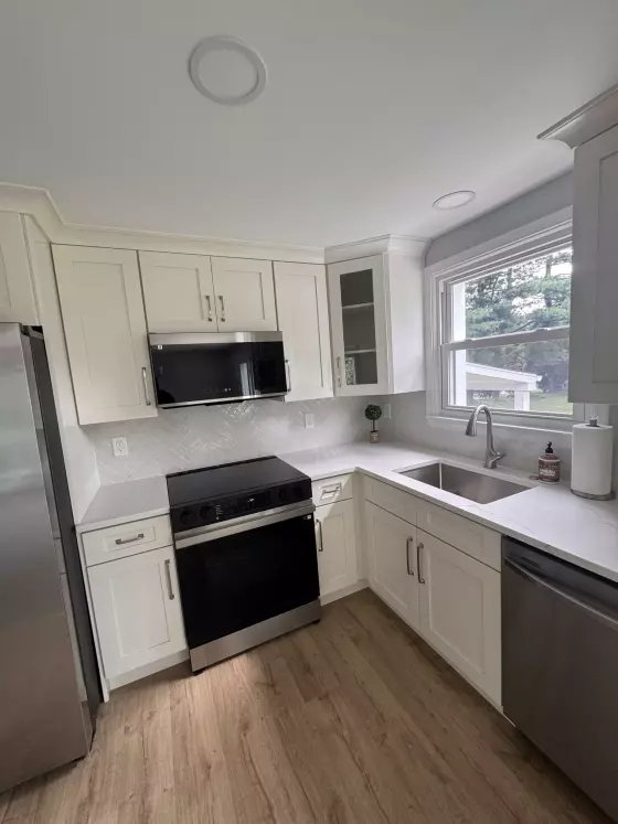 Cream shaker cabinets, glass-front cabinet, stainless range and microwave around a corner sink