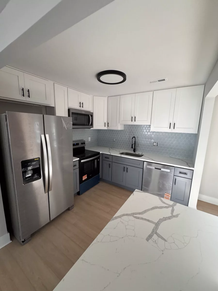 Kitchen with white upper and gray lower shaker cabinets, blue hexagon tile backsplash and a marble-look island