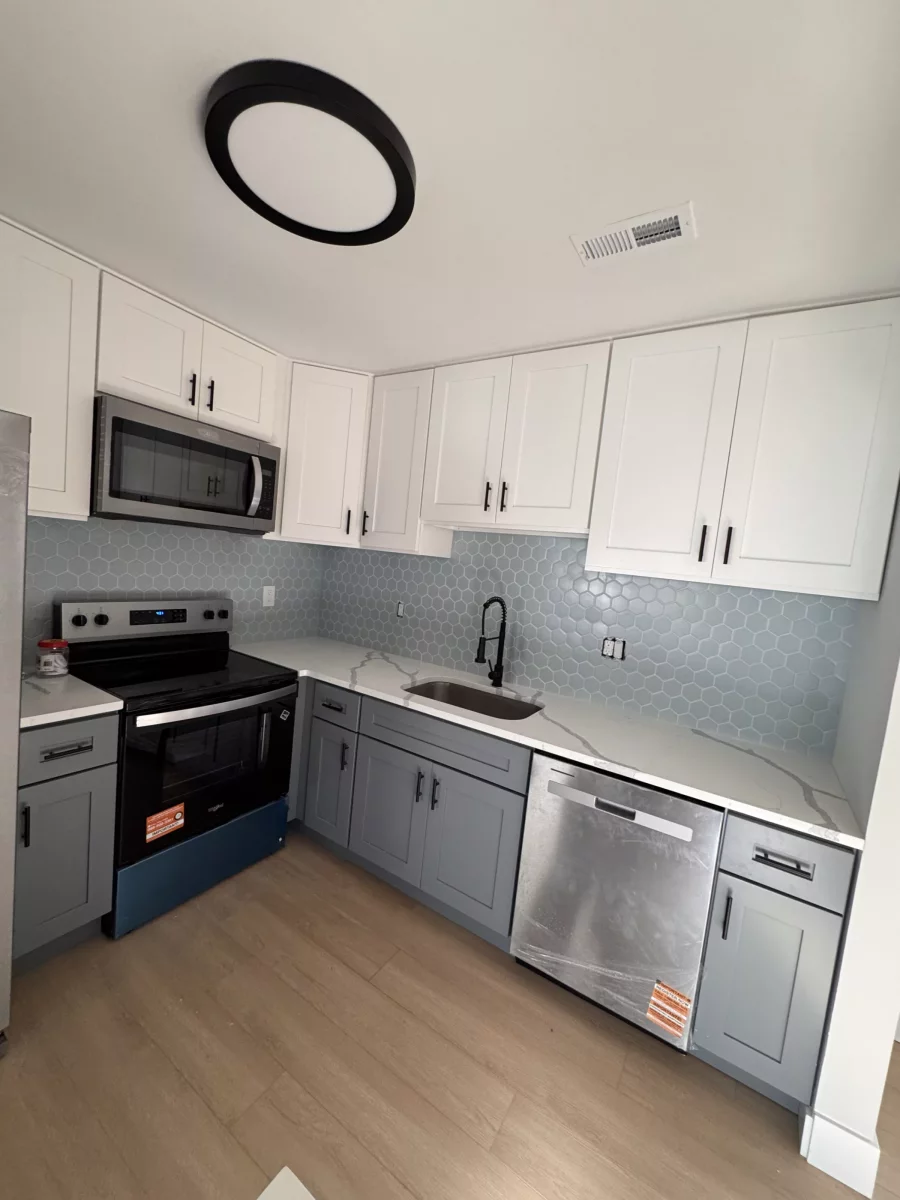 Gray lower cabinets, white uppers, blue hexagon tile backsplash and black faucet
