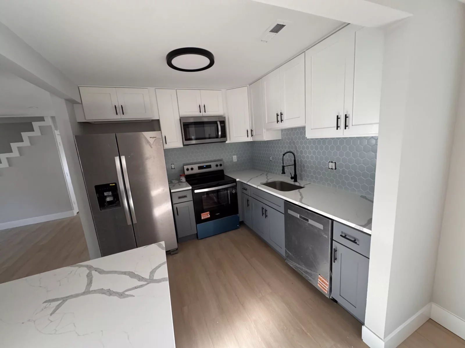 Two-tone kitchen with stainless refrigerator, range and dishwasher and a marble-look island top