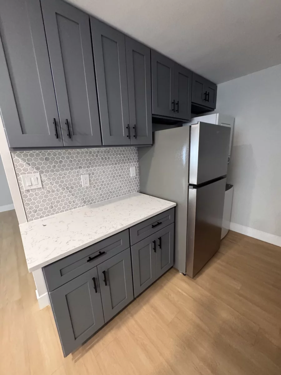 Gray shaker cabinets with black pulls, hexagon mosaic backsplash and stainless refrigerator
