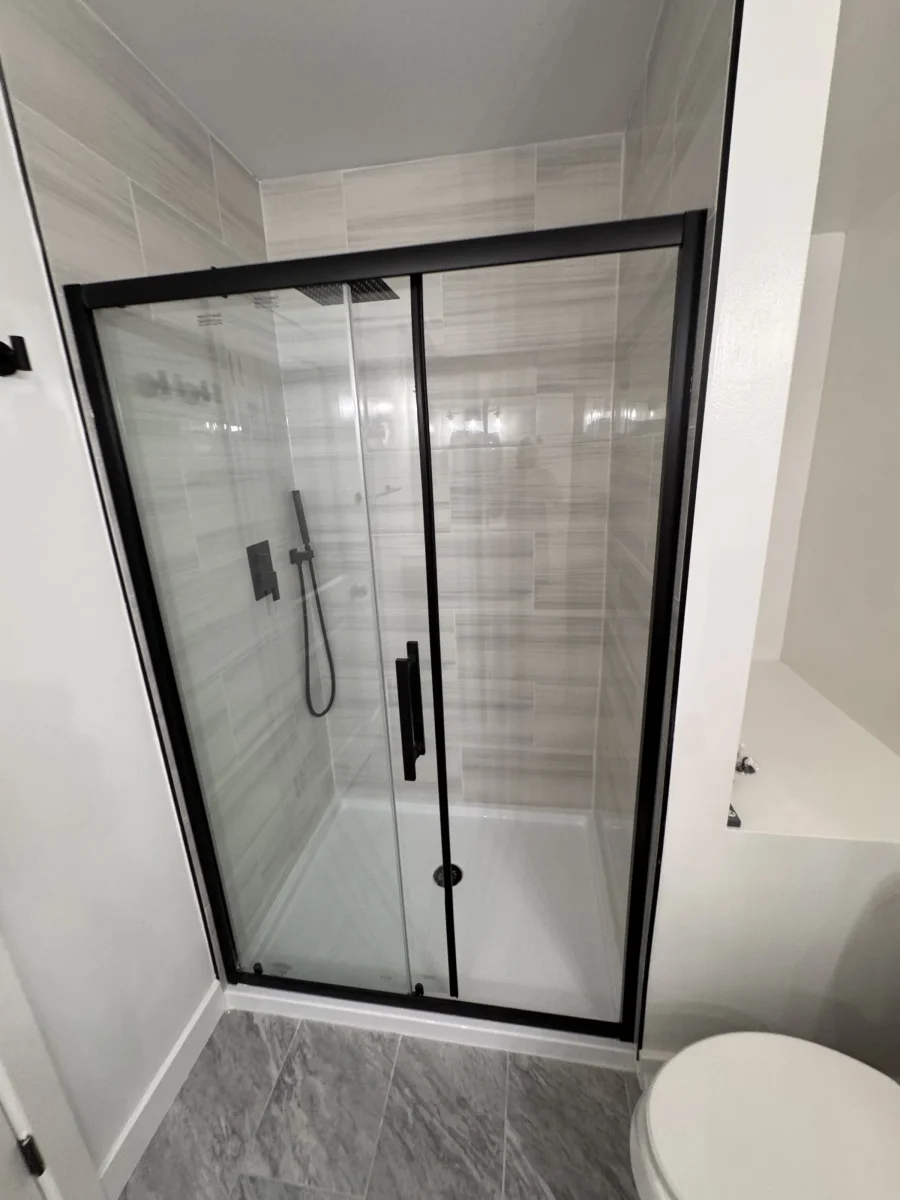 Walk-in shower with a black-framed glass door and stone-look tile