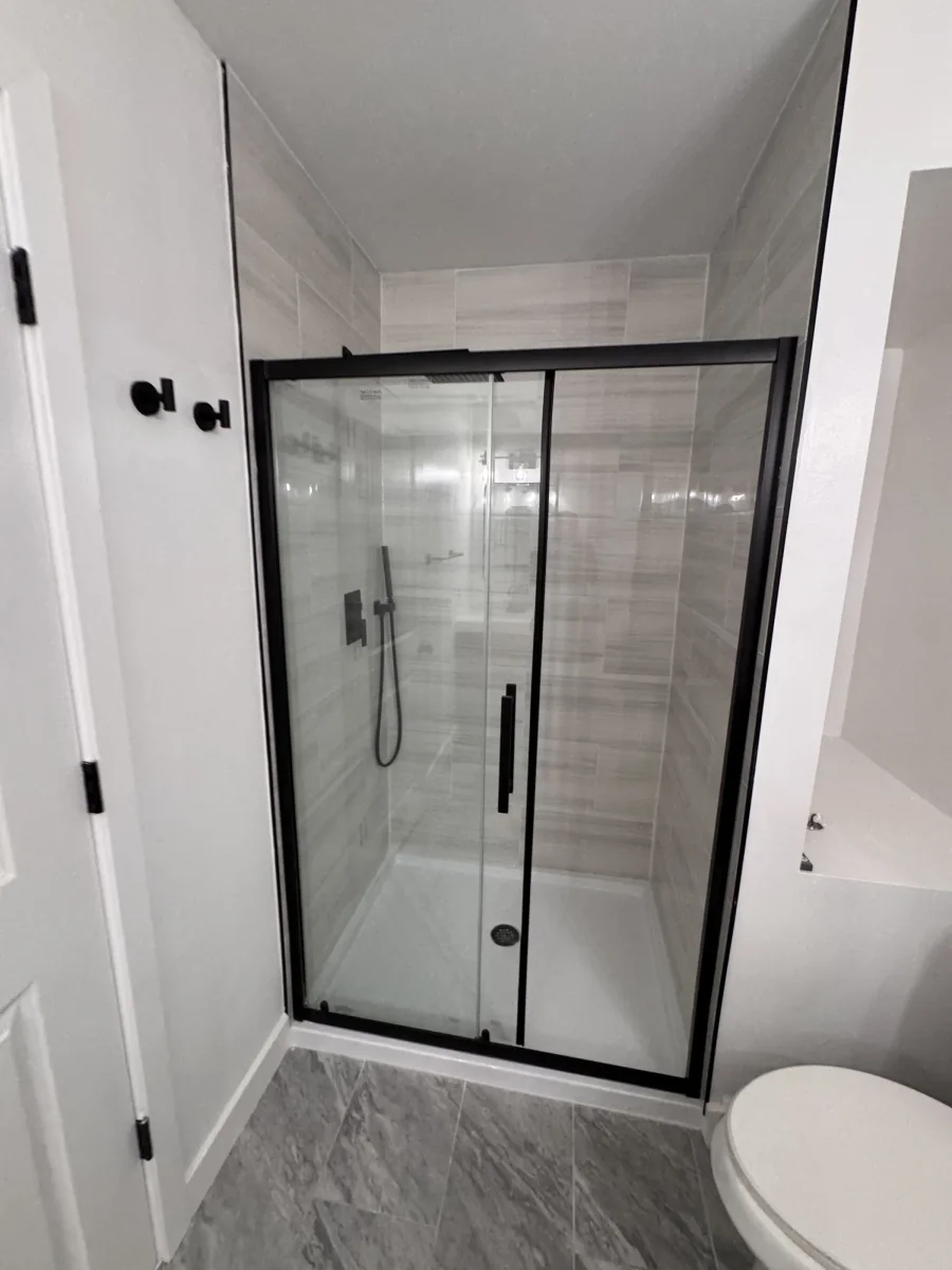 Walk-in shower behind a black-framed sliding glass door