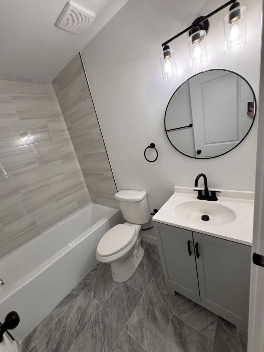 Gray vanity, round mirror and black vanity light next to the tub